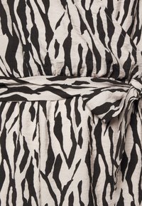 Robe portefeuille avec un motif zèbre noir et crème, en tissu texturé et avec un détail de taille nouée.