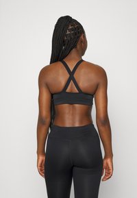 Sutien sport negru cu bretele intersectate, fabricat dintr-un material neted. Asortat cu colanți negri cu talie înaltă, evidențiind un design ajustat.