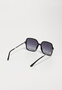 Ochelari de soare negri, cu lentile gri cu degradé, rame din plastic negru lucios și accente metalice argintii pe tâmple.