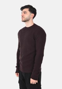 Maglione a coste di un viola scuro con scollo a girocollo, silhouette aderente e maniche allungate, indossato con pantaloni cargo neri.