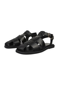 Sandalias de cuero negro con múltiples tiras entrecruzadas, diseño de punta abierta, correa ajustable en el tobillo con hebilla dorada, suela plana.