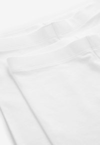 Shorts en coton blancs avec une texture lisse, présentant un design de ceinture uni, montrés sous un angle mettant en avant la douceur du tissu.