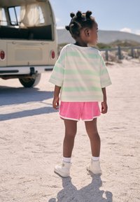 Light green and white striped oversized T-shirt, pink terrycloth shorts with white trim, and white high-top sneakers, standing on sandy ground.