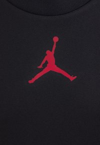 Černá látková košile s výrazným červeným logem Jumpman. Hladká textura, kulatý výstřih a přiléhavý střih.