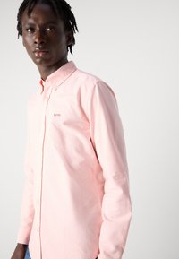 Camicia a maniche lunghe rosa chiaro con bottoni, realizzata in cotone, con un piccolo logo ricamato, colletto classico e una linea aderente.