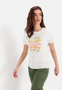 Witte t-shirt met een kleurrijke golf- en zonafbeelding in roze, oranje en groen. Heeft korte mouwen en een ronde halslijn. Groene broek.