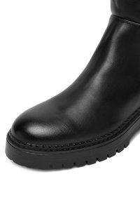 Gheată din piele neagră până la gleznă, cu vârf rotunjit, textură netedă și cusături contrastante de-a lungul tălpii. Talpa din cauciuc cu profil pentru aderență.