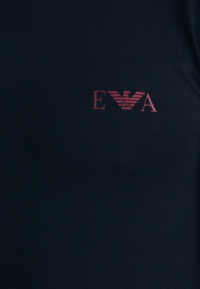 T-shirt ajustée bleu marine en tissu lisse, ornée d'un logo rouge avec un emblème d'aigle et les initiales "EVA" sur le côté supérieur gauche.