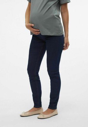 Matične jeans v temno modrem denimu z šivi, združeni z svetlo sivo majico in bež baletkami. Gladek, oprijet dizajn.