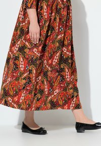 Czerwoną i czarną sukienkę maxi w wzór paisley o zwiewnym kroju, zestawioną z czarnymi lakierowanymi płaskimi butami z akcentem w postaci kokardy.
