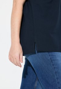 Top blu navy con maniche corte, dotato di una fessura laterale all'orlo, abbinato a jeans blu di media intensità. Tessuto morbido, vestibilità casual.
