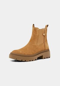 Botas de tobillo de ante marrón con un acabado texturizado, paneles laterales elásticos y una suela de goma gruesa con un diseño estriado.