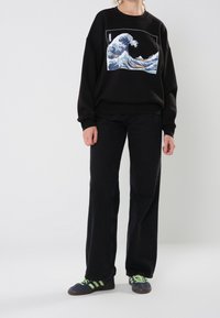 Černá mikina s modrobílým motivem vlny na přední straně, doplněná černými širokými kalhotami a modrými botami se zelenými detaily.