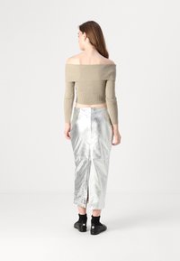 Beige off-the-shoulder ribbed crop top dan rok midi perak metalik dengan belahan belakang, dipadukan dengan sepatu hitam dan kaus kaki pergelangan kaki.