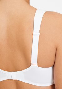 Witte beha met verstelbare bandjes en een gladde, naadloze band. De achterkant is rond en beschikt over een haak-en-oogsluiting.