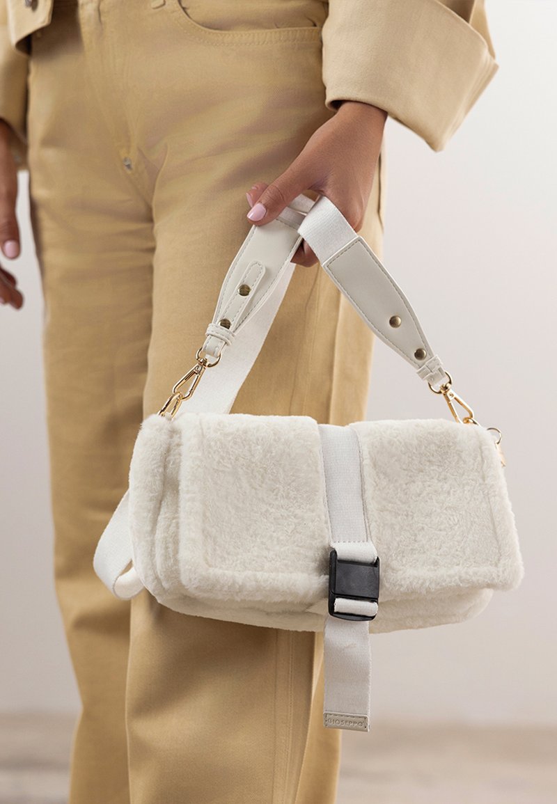 Bela torbica iz umetnega krzna z mehko teksturo, pravokotne oblike, s črno zaponko in odstranljivim belim trakom z zlatim okvirjem.