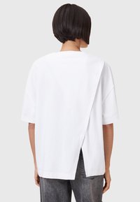 Witte katoenen T-shirt met een relaxte pasvorm, voorzien van een gespleten achterkant en korte mouwen. Gecombineerd met hooggelegen grijze denimjeans.