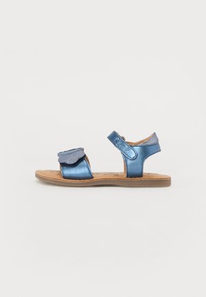 Blå metalliske sandaler med justerbar rem, dekorativ volang foran og brun flate såle. Lettere og åpent design.