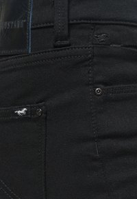 Juodos džinsinės kelnes su tekstūruotu audiniu, subtiliomis siūlėmis, logotipo etikete ir mažuoju žirgo emblemu šalia kišenės.