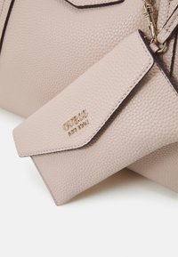 Sac à main en similicuir texturé rose clair avec des accents et marquage dorés. Doté d'un rabat et d'un design compact et structuré.