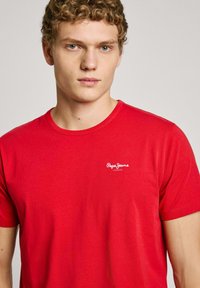 Raudona medvilnė t-shirt su apvaliu kaklu, su mažu baltu "Pepe Jeans London" logotipu kairėje krūtinės pusėje, lygios tekstūros, trumpomis rankovėmis.
