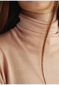 Jasnoróżowy sweter z golfem, wykonany z miękkiego, elastycznego materiału o gładkiej fakturze i subtelnie prążkowanym dekolcie.