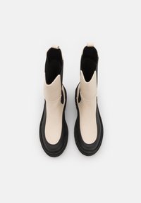 Un par de botas midi negras y beige con suelas negras gruesas, lengüetas en la parte trasera y paneles laterales elásticos, mostradas desde arriba sobre un fondo blanco.