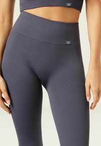 Gestreifte, hochtaillierte Leggings in Dunkelgrau, mit glatter Textur und Logopatch an der Taille. Figurbetontes Design, ideal für Sportbekleidung.