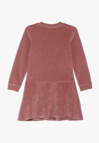 Růžové sametové šaty s dlouhým rukávem a rozšířenou sukní. Měkká textura, kulatý výstřih a přiléhavé manžety. Žádné viditelné vzory nebo kovové detaily.