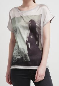 Camiseta de manga corta con un tejido semitransparente, que presenta una impresión fotográfica en blanco y negro. Cuello redondo, corte holgado, textura suave.