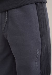 Pelēki sporta bikses ar strukturētām sānu paneļiem, regulējamu auklu un drukātu "BLUE RIDGE DENIM" etiķeti. Mīksta auduma, ērtas piegulšanas.
