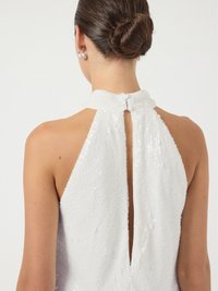 Λευκό φόρεμα με παγιέτες που διαθέτει ψηλό λαιμό, άνοιγμα στην πλάτη και υφή στην επιφάνεια. Το υλικό ανακλά το φως με ομαλή πτώση.