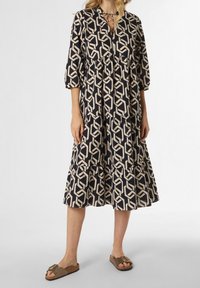 Laivastonsininen mekko, jossa on beigecoloreinen geometrinen kuvio, löysä malli, kolmanneksen pituiset hihat ja kerroksellinen röyhelöhelma. Yhdistetty ruskeisiin sandaaleihin.