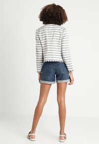 Giacca a righe in tessuto grigio e bianco con orlo sfilacciato, abbinata a pantaloni shorts in denim con risvolti e tasche posteriori.