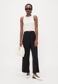 Hvit kort topp, svarte vide bukser, hvite slingback-sko og en kremfarget håndveske. Har minimalistisk design og glatte teksturer.