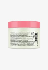 Kokosnøtt kroppsskrubb i en rund klar krukke med rosa lokk. Teksturerte etiketter viser bruksanvisning og ingrediensliste på flere språk.