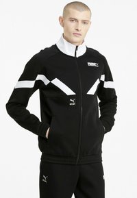 Fekete zipzáros dzseki fehér és szürke átlós díszítéssel, texturált anyagból készült. Puma logóval és oldalzsebekkel rendelkezik. Hozzá illő fekete nadrág.