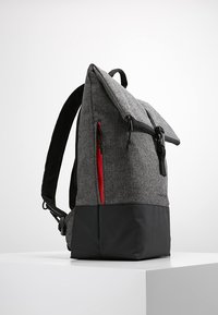 Zaino a spina di pesce grigio con parte inferiore nera, chiusura a pattina superiore e dettaglio zip rossa sul lato. Spallacci imbottiti visibili.