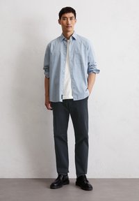 Light blue checkered button-up shirt, white t-shirt underneath, dark pants, black shoes. The shirt has a pocket and rolled sleeves.