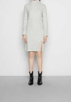 Robe en tricot côtelé grise avec un col montant et une fente jusqu'à la cuisse ; associée à des bottines en cuir noir à bout ouvert.