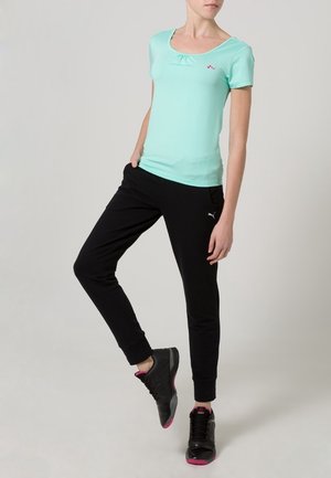 Ljusmintgrön kortärmad topp med rynkad halsringning, ihop med svarta sweatpants med en logotyp på vänstra låret och muddar. Svarta sneakers med rosa detaljer.