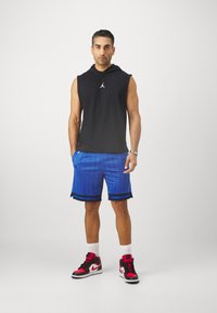 Fekete ujjatlan kapucnis pulcsi fehér logóval, kék csíkos sortok és piros/fekete sportcipők. Az öltözet sportos, modern dizájnnal rendelkezik.