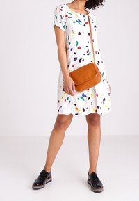 Hvid kortærmet kjole med et farverigt abstrakt mønster, parret med en brun crossbody taske og sorte snørebåndssko.