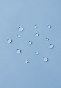 Picături de apă clare, de dimensiuni variate, pe o suprafață netedă de culoare albastru deschis, creând un contrast cu textura de dedesubt.