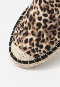 Espadrille à imprimé léopard avec une tige en toile texturée, un bord noir et une semelle en jute tressé présentant des détails de couture contrastés.