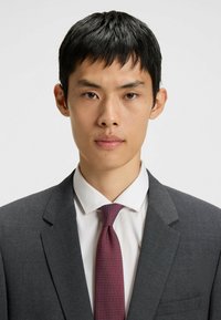 Gray suit jacket over a white shirt, complemented by a maroon tie with small white dots. Smooth textures and tailored design.