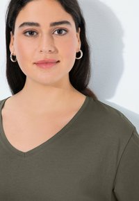 Olive green v-neck top in soft fabric with short sleeves. Features a relaxed fit and minimal stitching details, enhancing its simplicity.