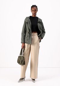 Veste olive avec capuche, crop top noir et pantalons beige à jambe large. Accessoirisée avec un sac vert olive et des talons argentés.