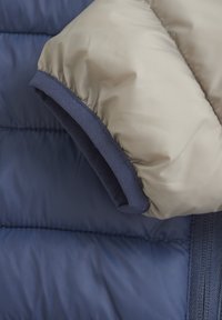 Giubbotto puffer con maniche in tessuto lucido beige a bordi blu navy e corpo in blu navy testurizzato. Presenta dettagli cuciti e polsini.