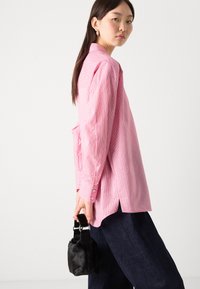Pink striped shirt with buttoned cuffs, paired with dark blue wide-leg trousers; model holds a small black fur handbag.